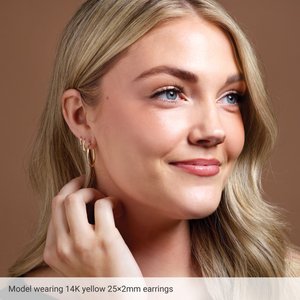 Model wearing 25 mm classic 2 mm tube hoop earrings in 14K yellow gold